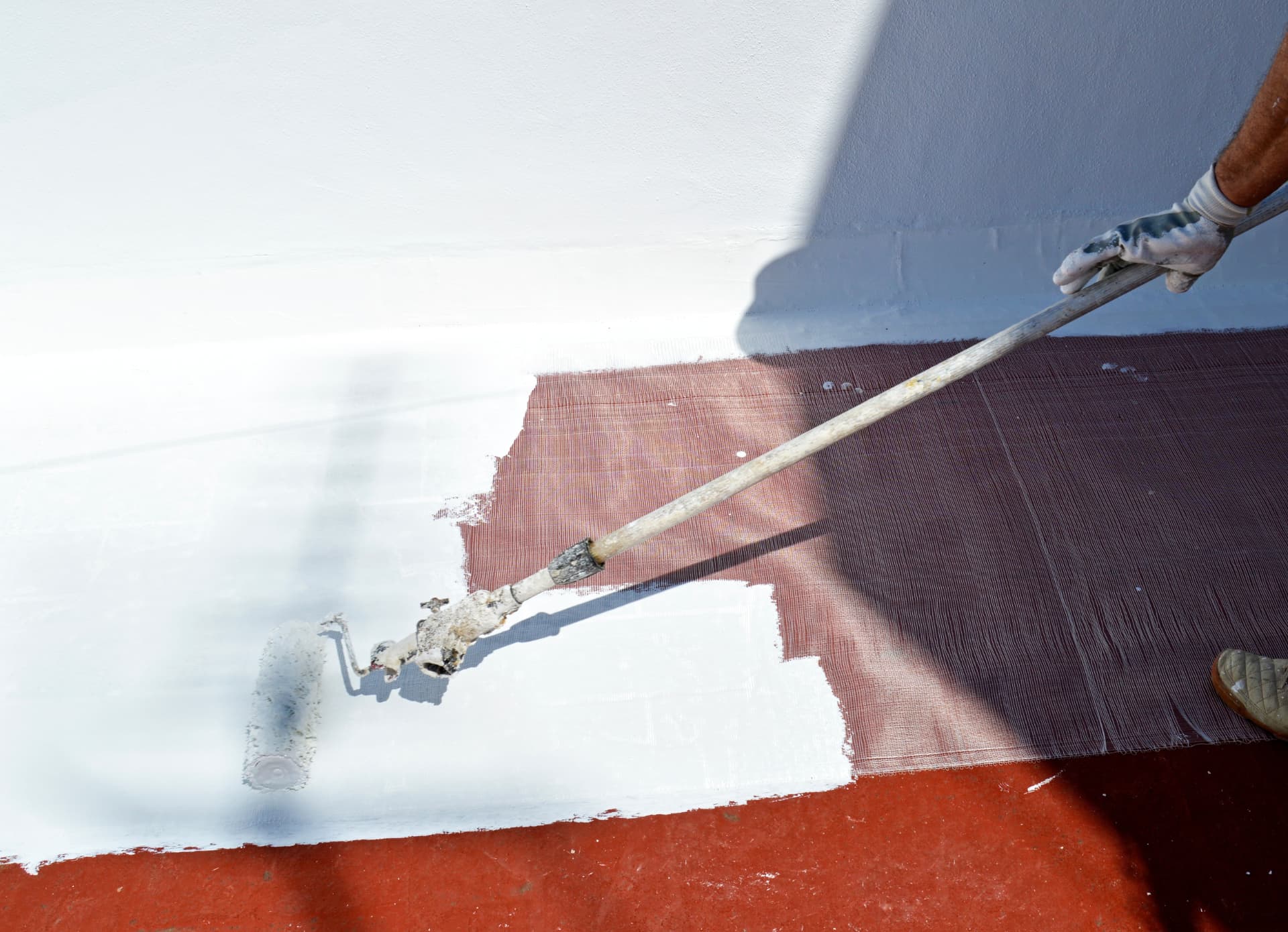 Reinforced liquid waterproofing being roller-applied over a roof deck